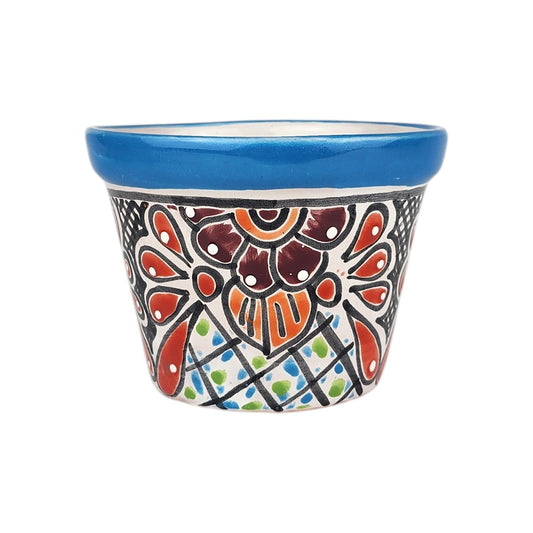 A small hand-painted ceramic pot with a vibrant blue rim and a colorful, intricate floral pattern on a white background.
