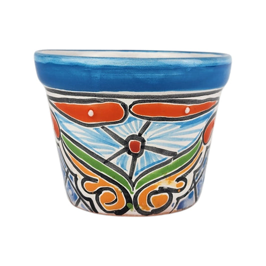A small hand-painted ceramic planter pot with a vibrant blue rim and a colorful hand-painted floral and scroll pattern in orange, green, white, and black on a white background.