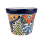 A hand-painted ceramic planter pot with a white base, featuring a vibrant Mexican Talavera style design with blue, orange, green, and red floral and geometric patterns, and a glossy dark blue rim.