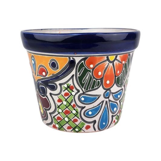 A hand-painted ceramic planter pot with a white base, featuring a vibrant Mexican Talavera style design with blue, orange, green, and red floral and geometric patterns, and a glossy dark blue rim.