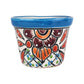 A small hand-painted ceramic pot with a vibrant blue rim and a colorful floral pattern in orange, red, brown, green, and blue on a white background, isolated on a white studio background.