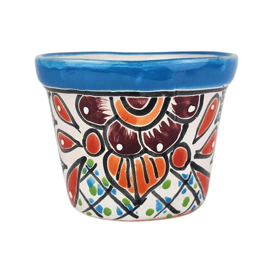 A small hand-painted ceramic pot with a vibrant blue rim and a colorful floral pattern in orange, red, brown, green, and blue on a white background, isolated on a white studio background.