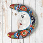 Red Talavera-style ceramic moon wall décor with colorful floral patterns on rustic white wood background