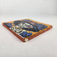 Angled view of golden yellow Catrina Portrait ceramic tile showing glossy surface and natural terracotta edges