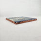 Angled view of blue Catrina Portrait ceramic tile showing glazed surface and natural terracotta edges