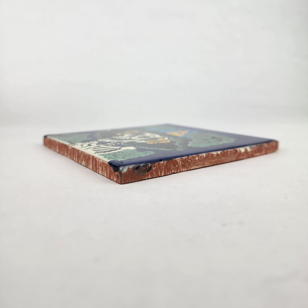 Angled view of blue Catrina Portrait ceramic tile showing glazed surface and natural terracotta edges