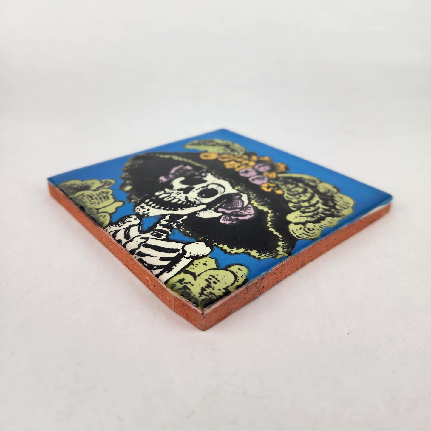 Angled view of sky blue Catrina Portrait ceramic tile showing glossy surface and natural terracotta edges