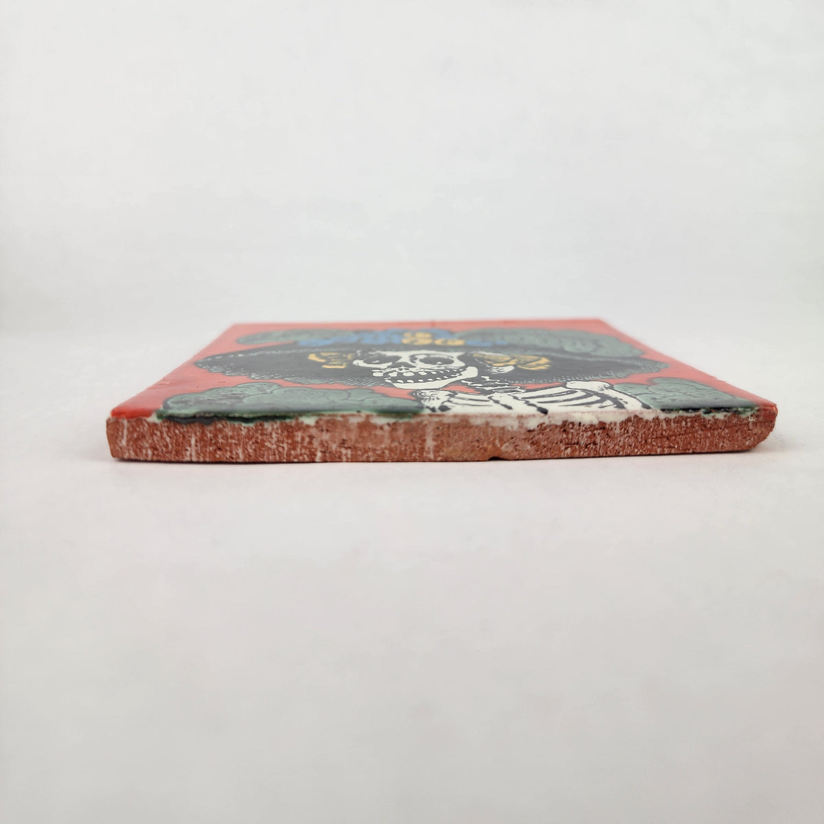 Red orange Catrina Portrait ceramic tile shown from front edge highlighting ceramic thickness and natural terracotta edge