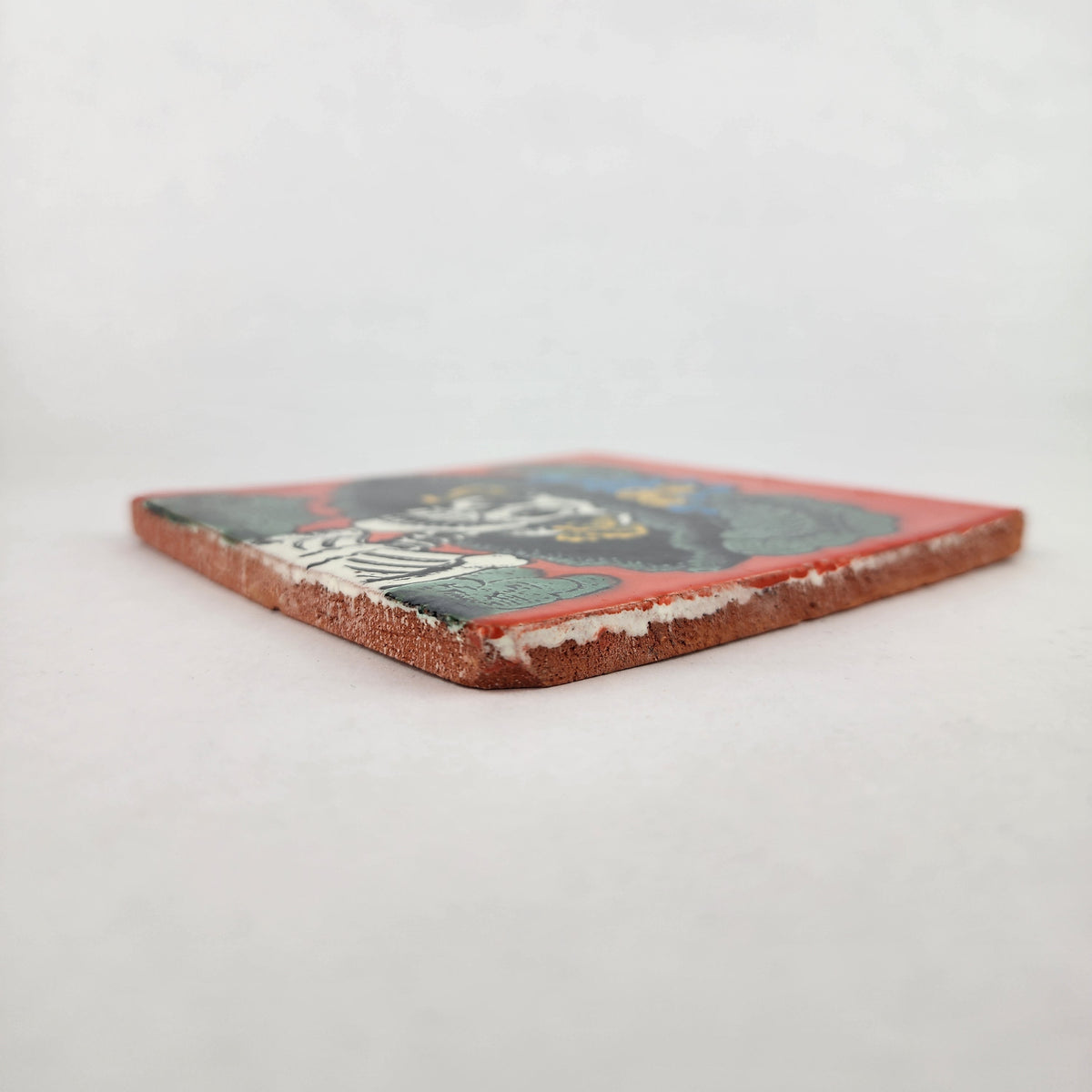 Angled view of red orange Catrina Portrait ceramic tile showing glossy surface and natural terracotta edges