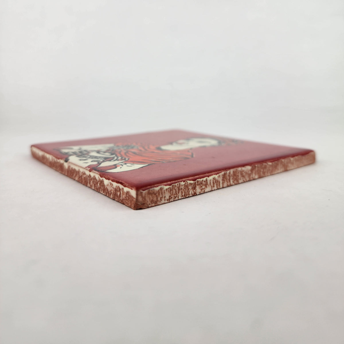 Angled view of brick red Frida Kahlo portrait ceramic tile showing glossy surface and terracotta edges