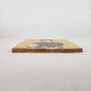 Mustard yellow Frida Kahlo ceramic tile shown from front edge highlighting ceramic thickness and terracotta edge