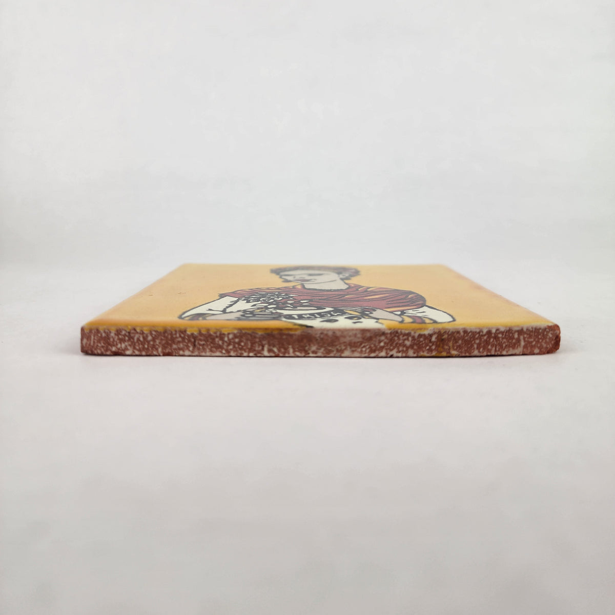 Mustard yellow Frida Kahlo ceramic tile shown from front edge highlighting ceramic thickness and terracotta edge
