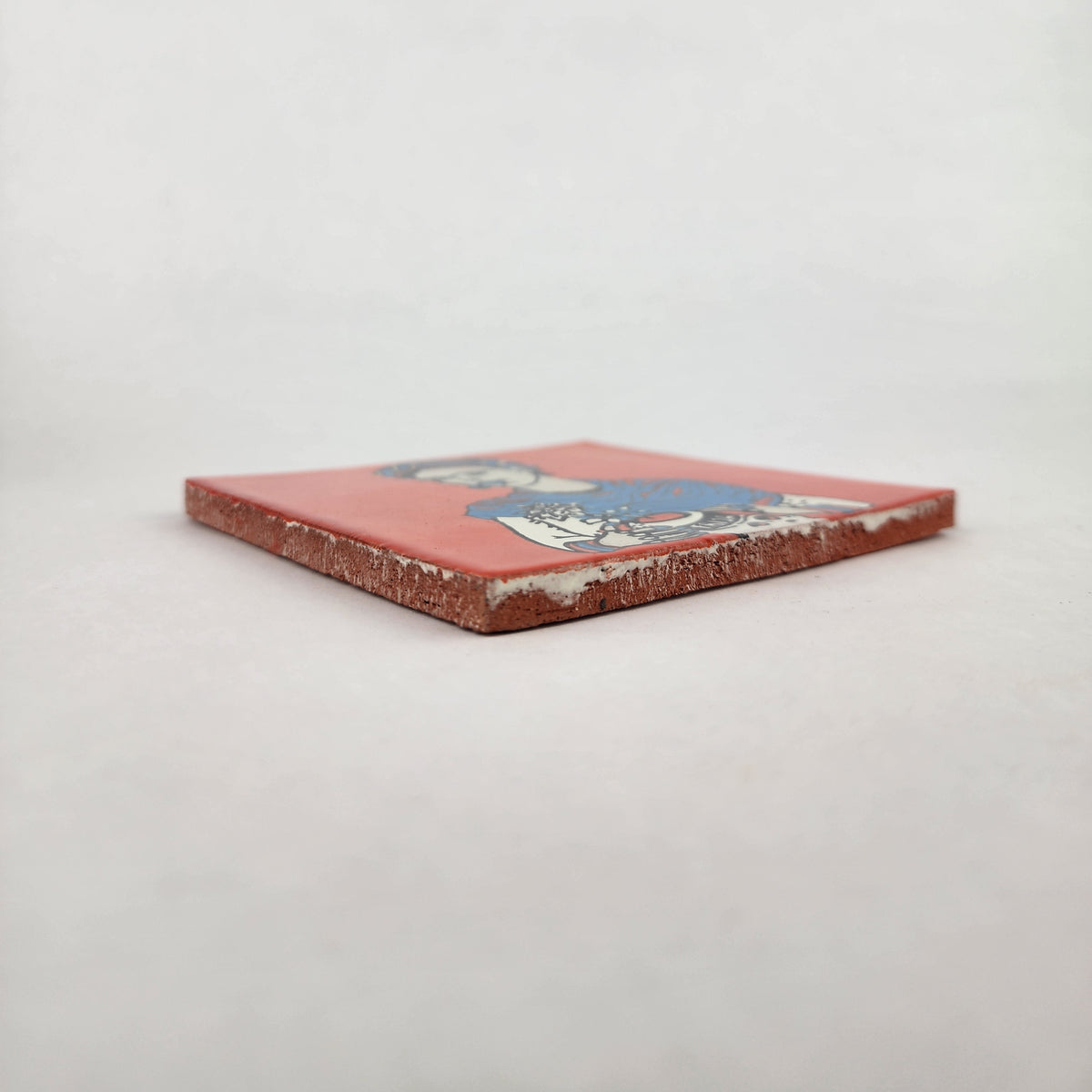 Angled view of red orange Frida Kahlo portrait ceramic tile showing glazed surface and ceramic edge