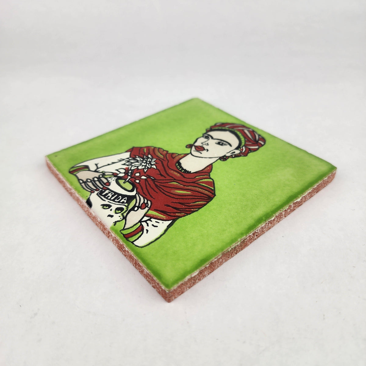 Angled view of lime green Frida Kahlo portrait ceramic tile showing glossy surface and natural terracotta edges