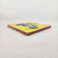 Angled view of Skeleton Motorcycle ceramic tile with yellow background showing glazed surface and ceramic edge