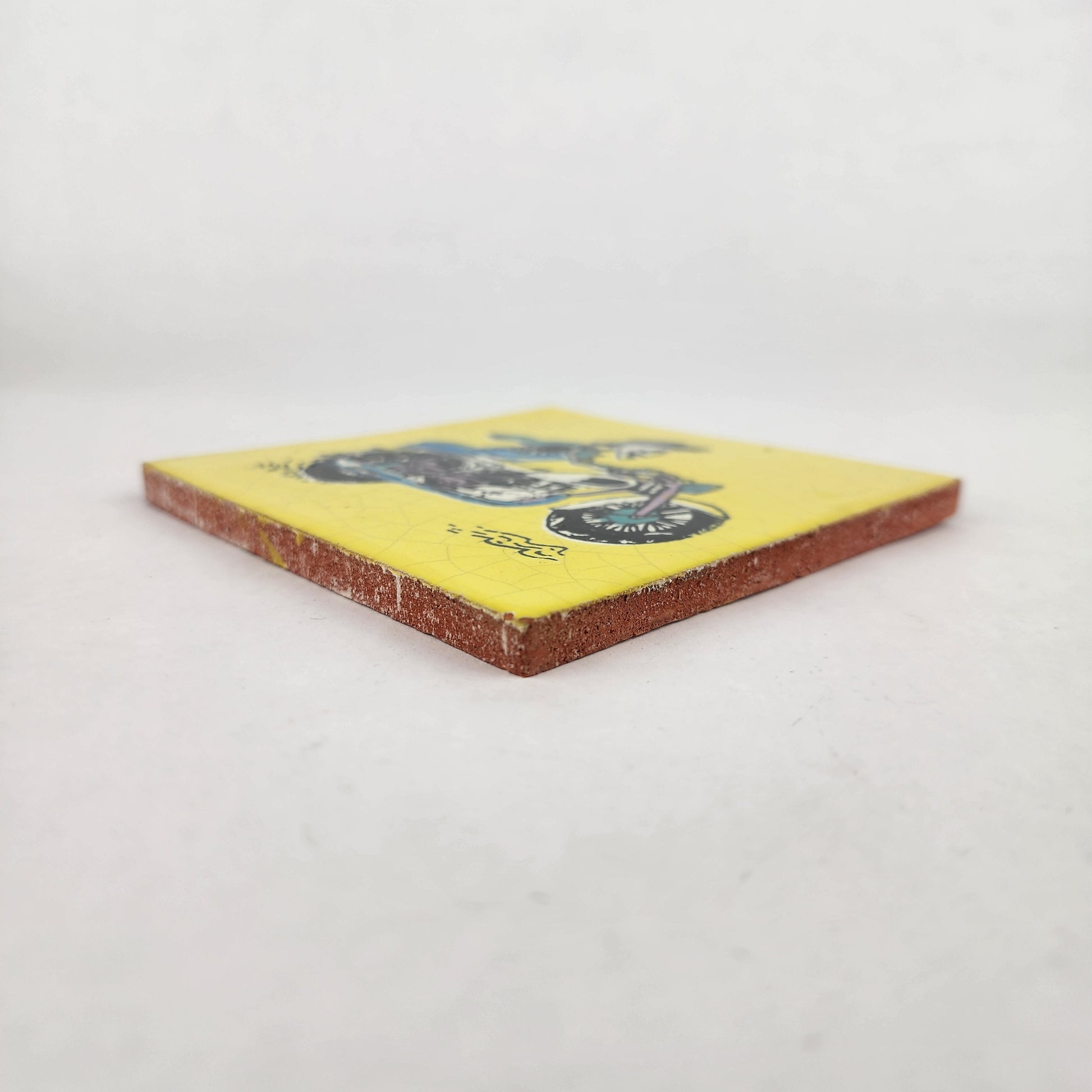 Angled view of Skeleton Motorcycle ceramic tile with yellow background showing glazed surface and ceramic edge