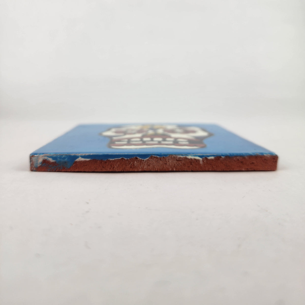 Side view of 4 1/8 inch floral sugar skull ceramic tile showing thickness and unfinished clay edge