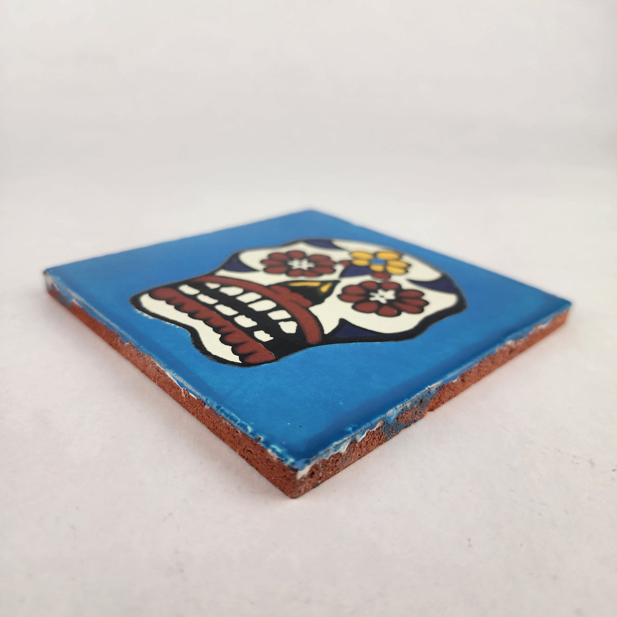Angled view of sky blue Mexican ceramic tile with colorful floral sugar skull design