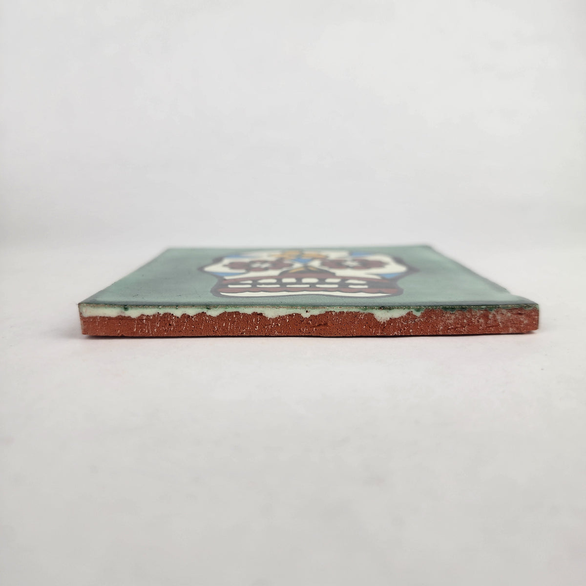 Side view of 4 1/8 inch floral sugar skull ceramic tile showing thickness and glazed edge