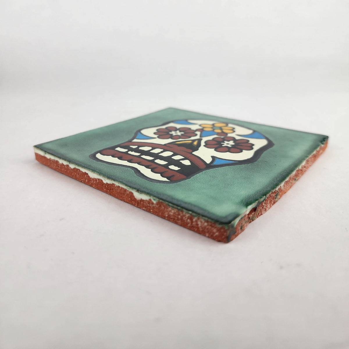 Angled view of green Mexican ceramic tile with colorful floral sugar skull design