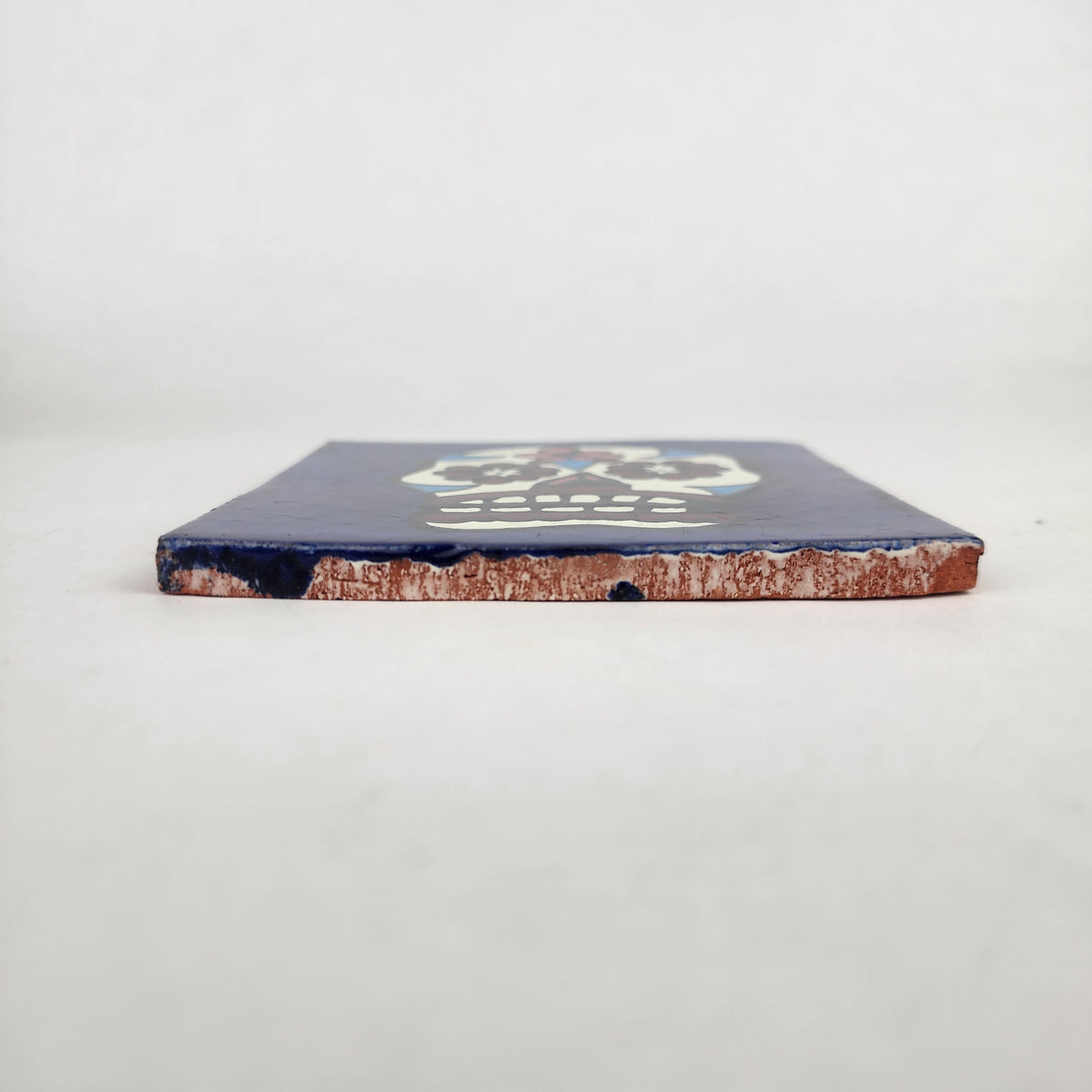 Side view of 4 1/8 inch floral sugar skull ceramic tile showing thickness and glazed edge