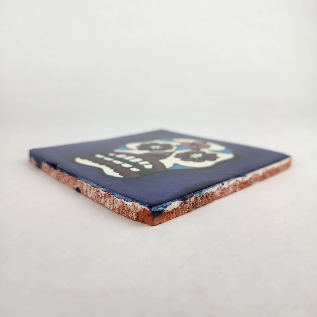 Angled view of royal blue Mexican ceramic tile with colorful floral sugar skull design