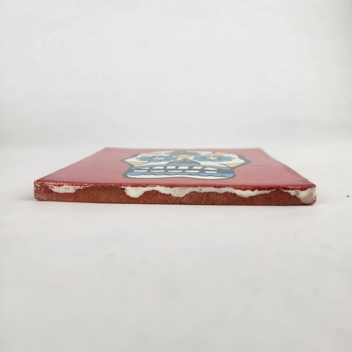 Side view of 4 1/8 inch floral sugar skull ceramic tile showing thickness and glazed edge