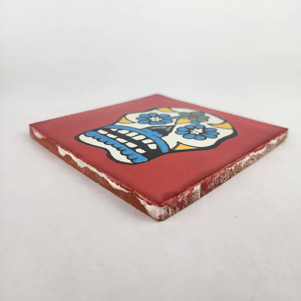Angled view of red Mexican ceramic tile with colorful floral sugar skull design