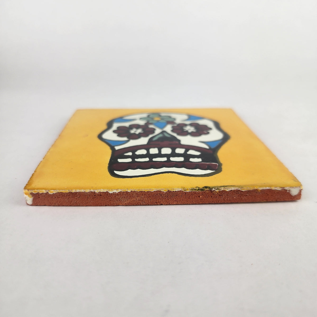 Side view of 4 1/8 inch floral sugar skull ceramic tile showing thickness and glazed edge