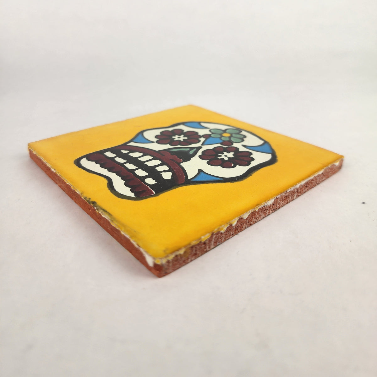 Angled view of mustard yellow Mexican ceramic tile with colorful floral sugar skull design