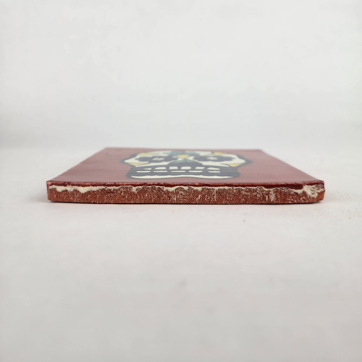 Side view of 4 1/8 inch floral sugar skull ceramic tile showing thickness and glazed edge