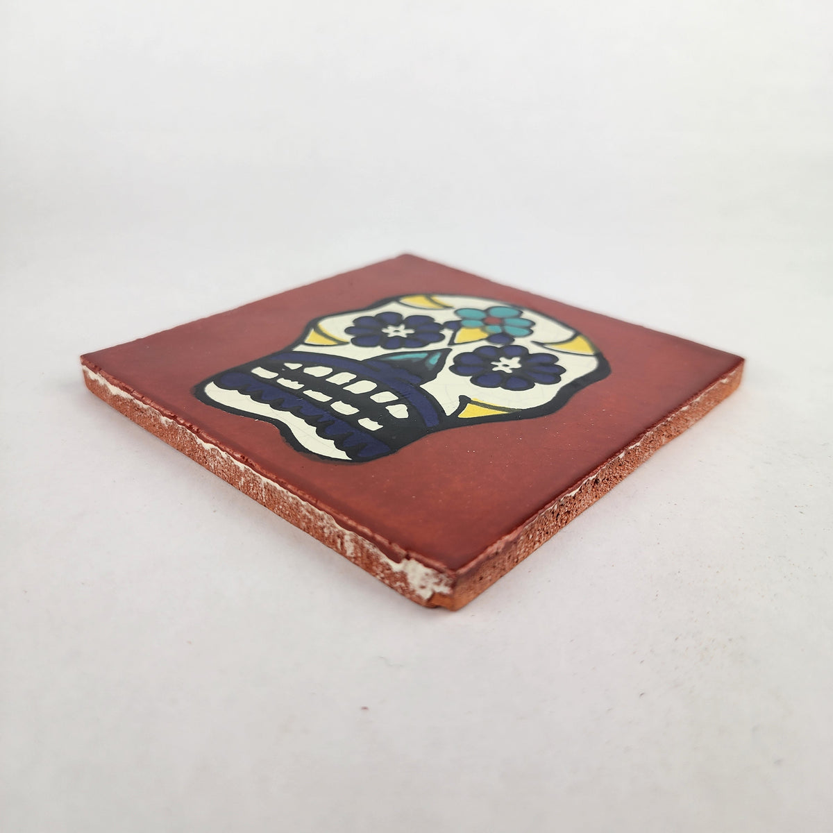 Angled view of red-brown Mexican ceramic tile with colorful floral sugar skull design