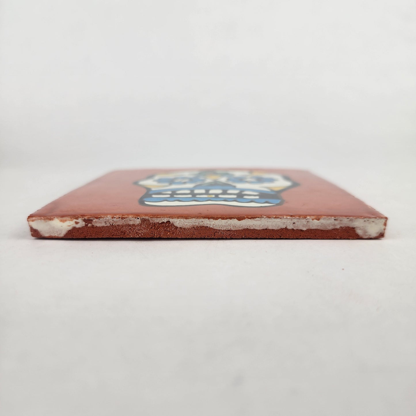 Side view of 4 1/8 inch floral sugar skull ceramic tile showing thickness and glazed edge