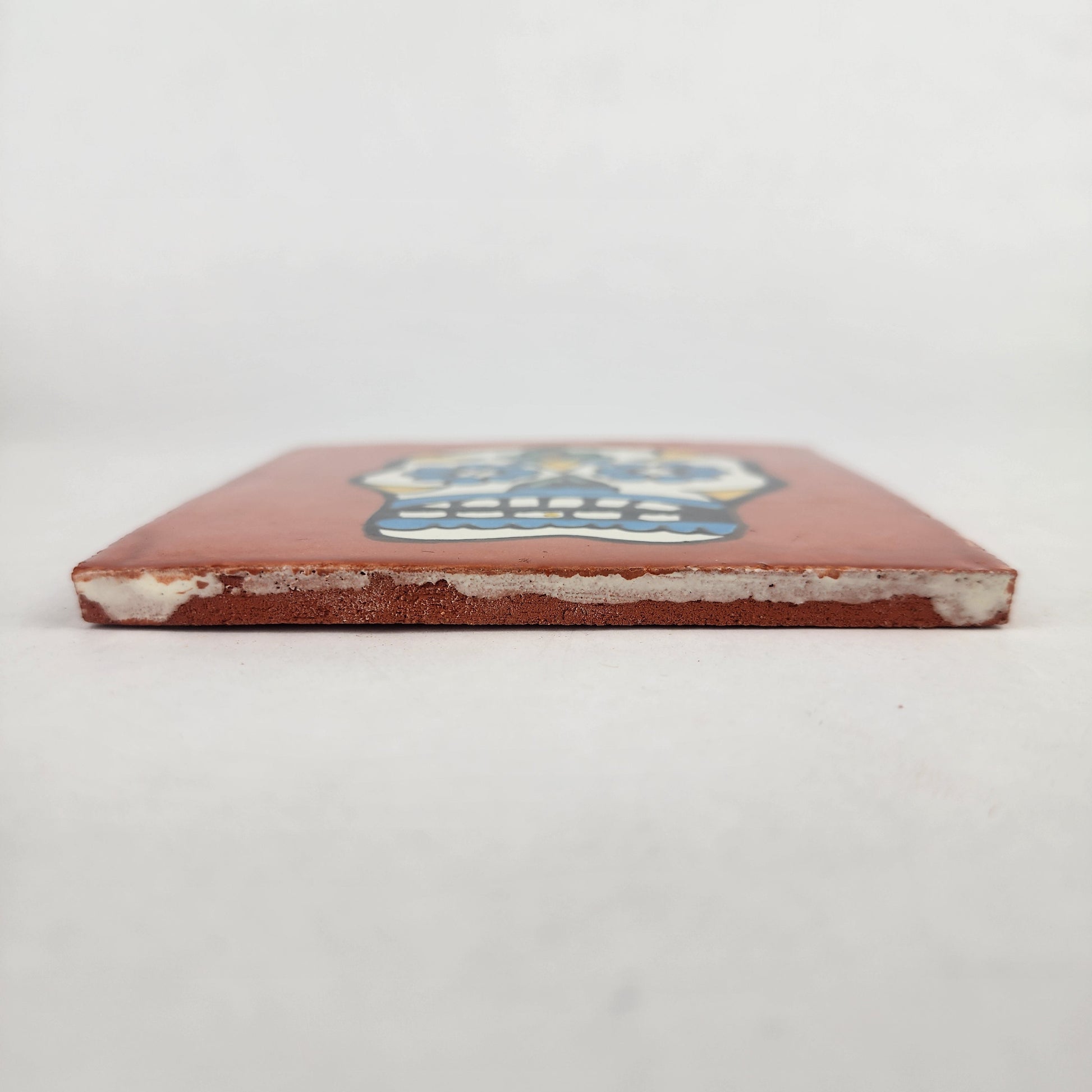 Side view of 4 1/8 inch floral sugar skull ceramic tile showing thickness and glazed edge