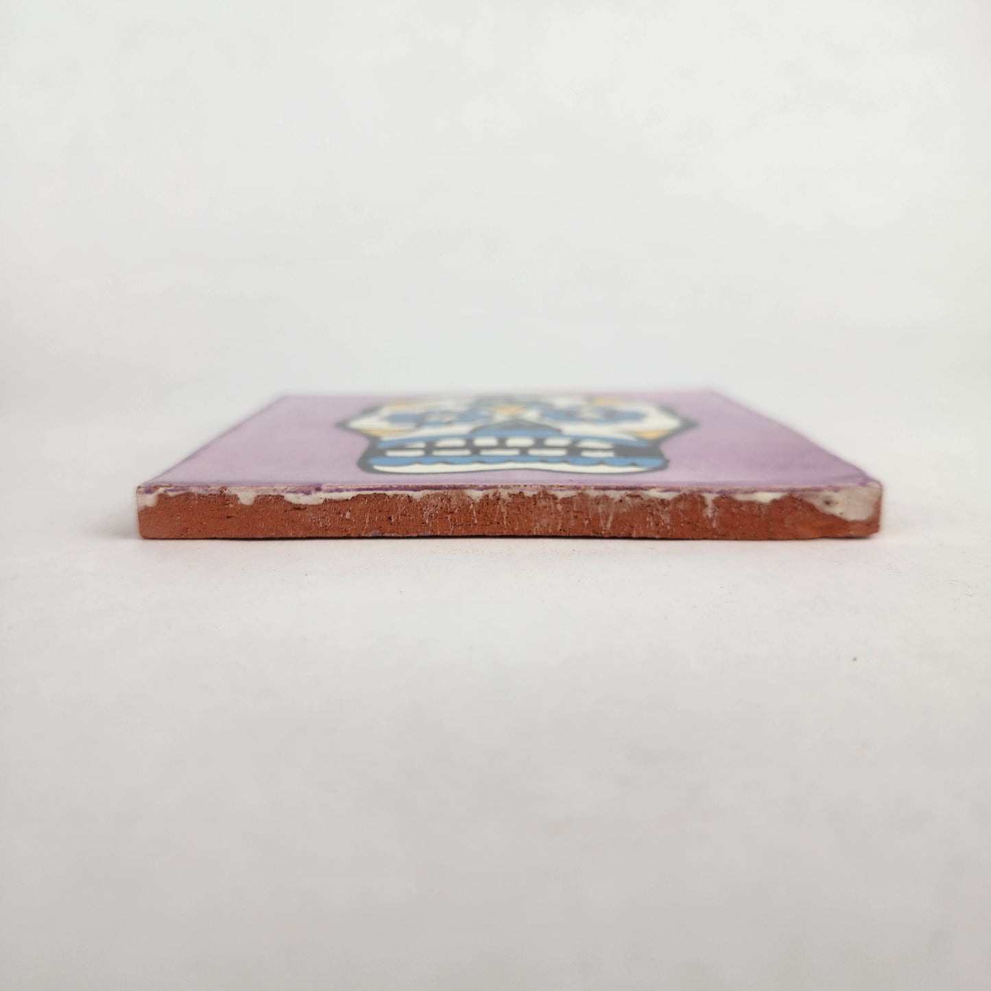Side view of 4 1/8 inch floral sugar skull ceramic tile showing thickness and glazed edge