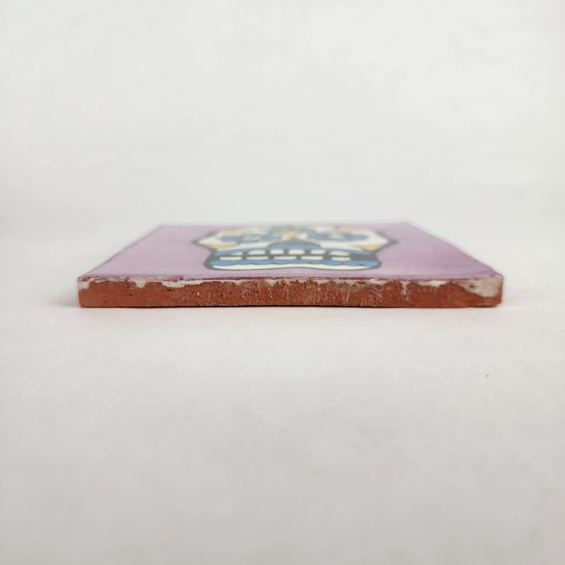 Side view of 4 1/8 inch floral sugar skull ceramic tile showing thickness and glazed edge
