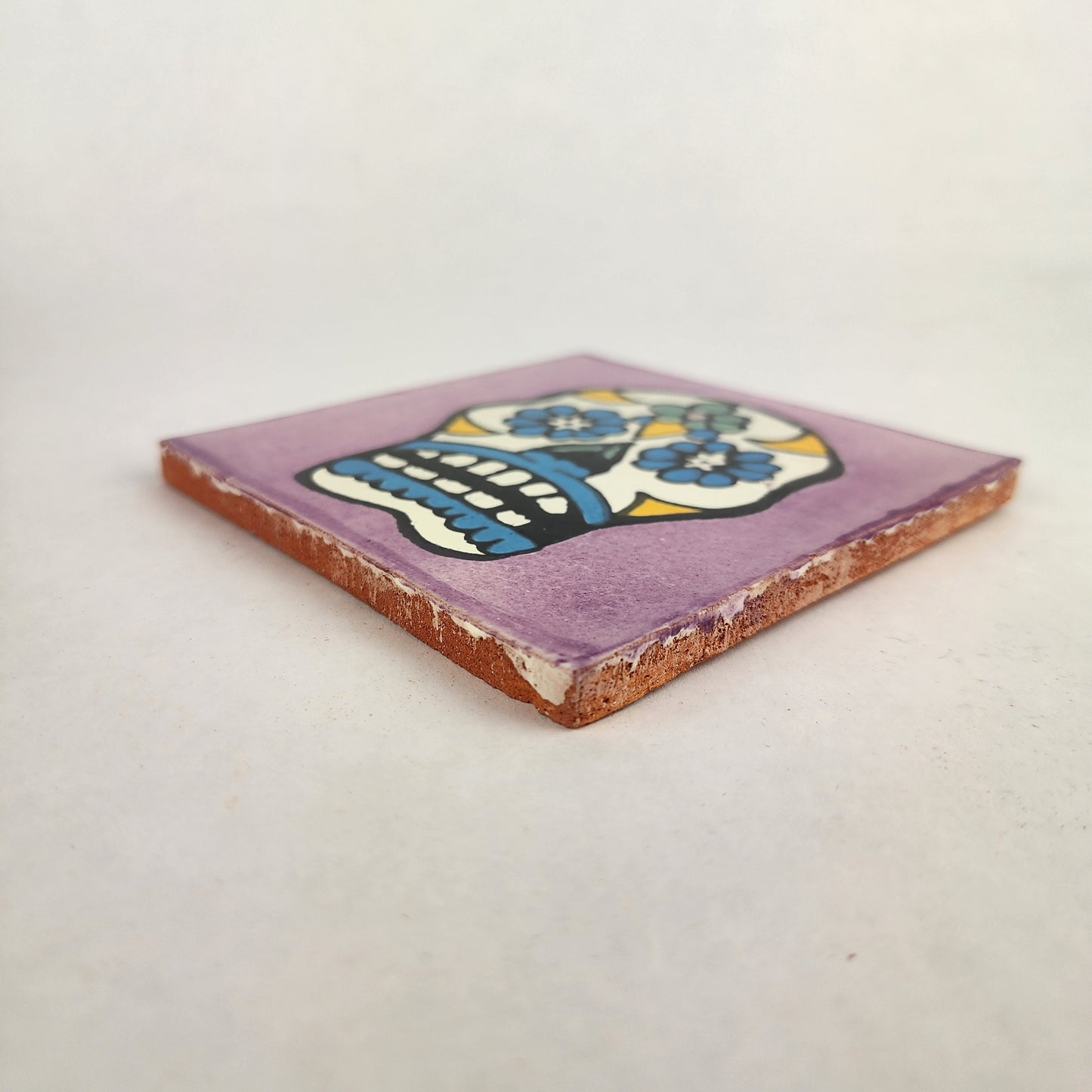 Angled view of purple Mexican ceramic tile with colorful floral sugar skull design