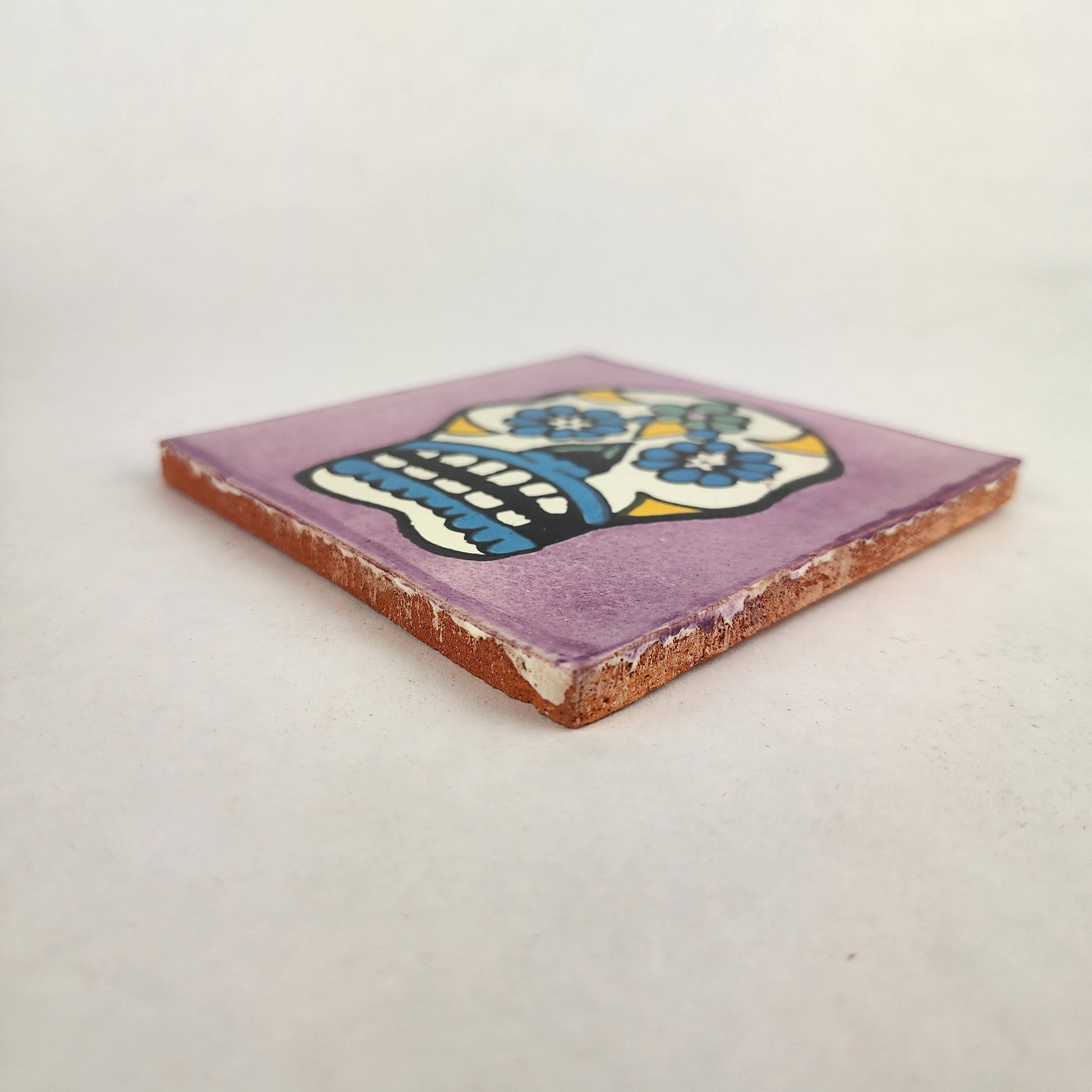 Angled view of purple Mexican ceramic tile with colorful floral sugar skull design