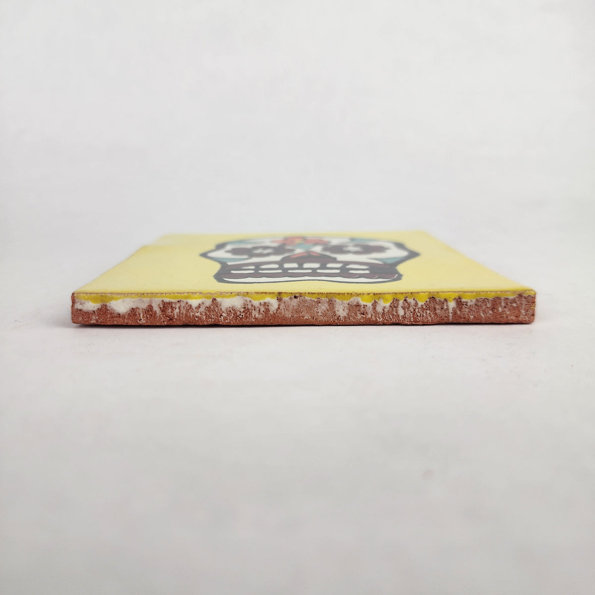 Side view of 4 1/8 inch floral sugar skull ceramic tile showing thickness and unfinished clay edge