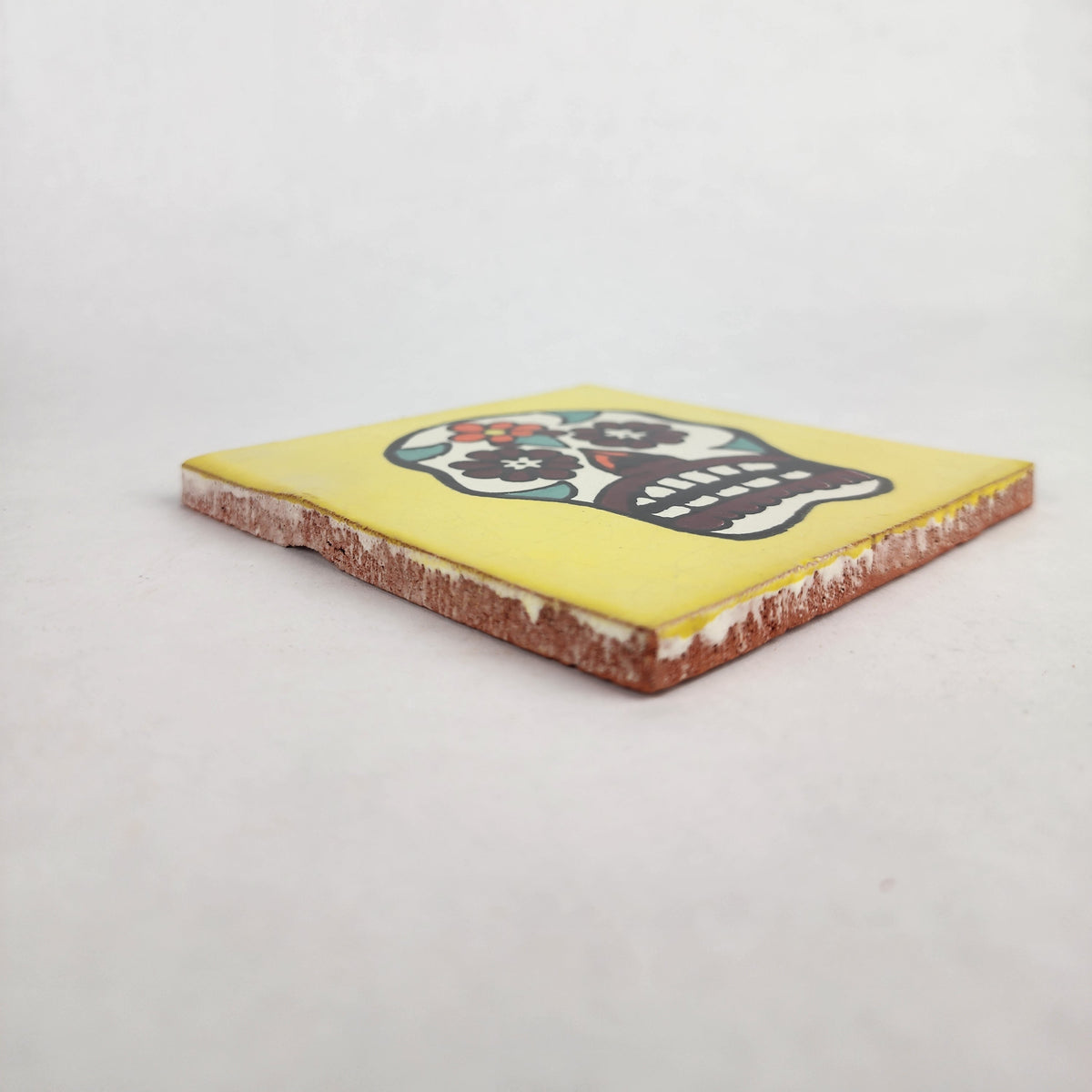 Angled view of yellow Mexican ceramic tile with colorful floral sugar skull design
