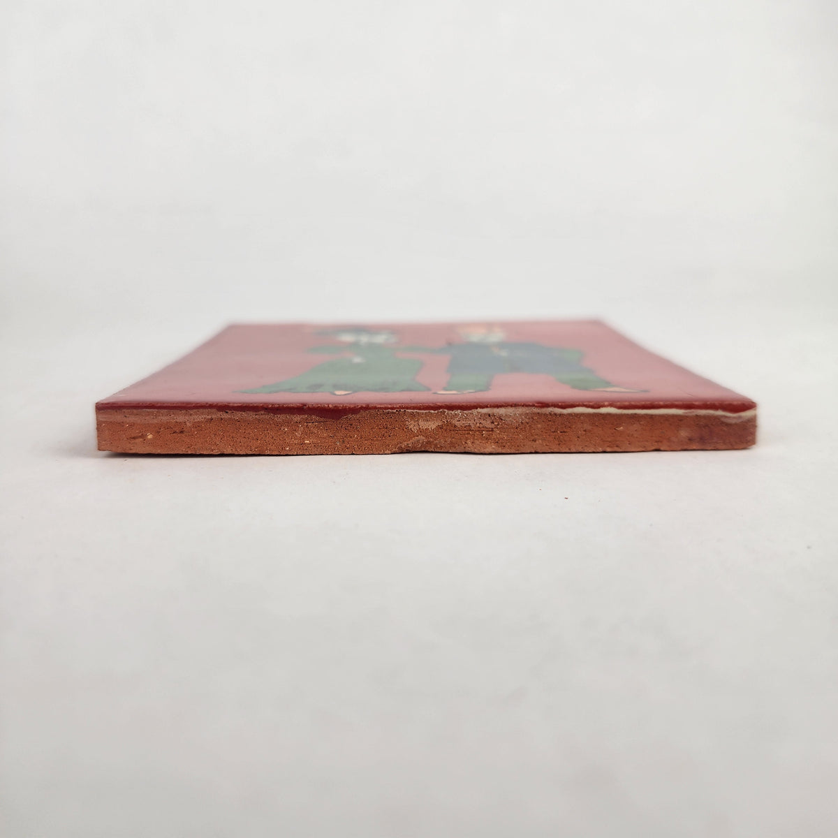 Side view of red Skeleton Couple ceramic tile showing glazed surface and terracotta edge