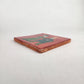 Angled view of red Skeleton Couple ceramic tile showing glossy finish and terracotta edges