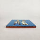 Side view of blue Skeleton Couple ceramic tile showing glazed surface and terracotta edge