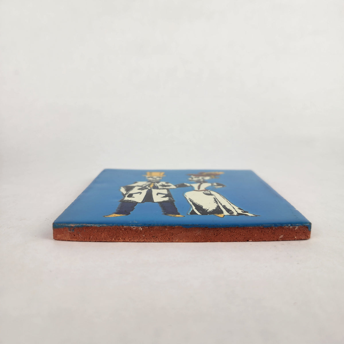 Side view of blue Skeleton Couple ceramic tile showing glazed surface and terracotta edge
