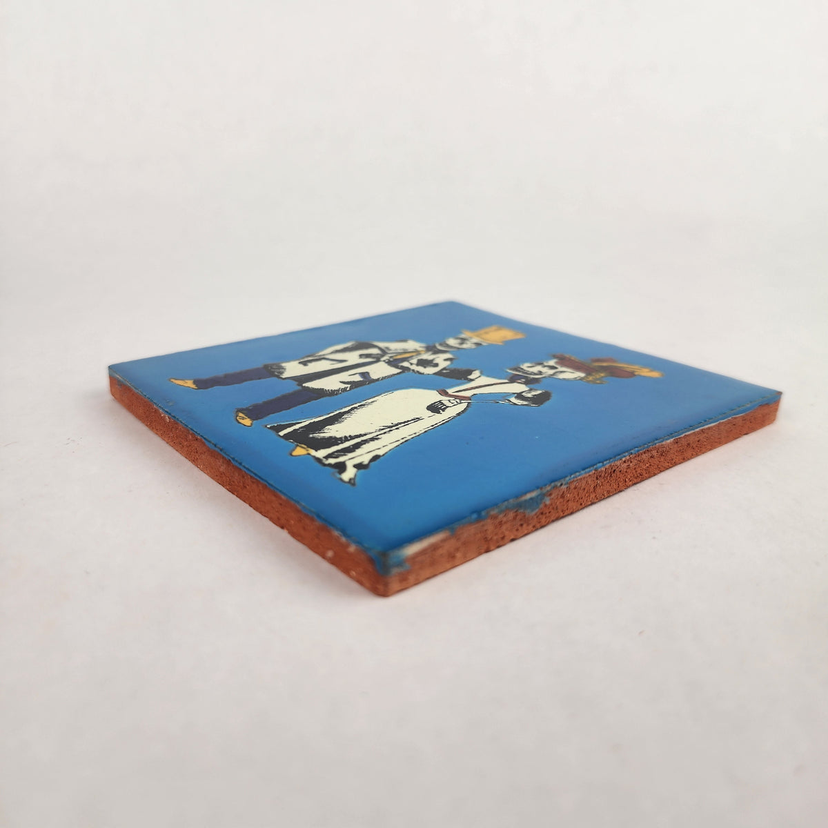 Side view of blue Skeleton Couple ceramic tile showing glazed surface and terracotta edge