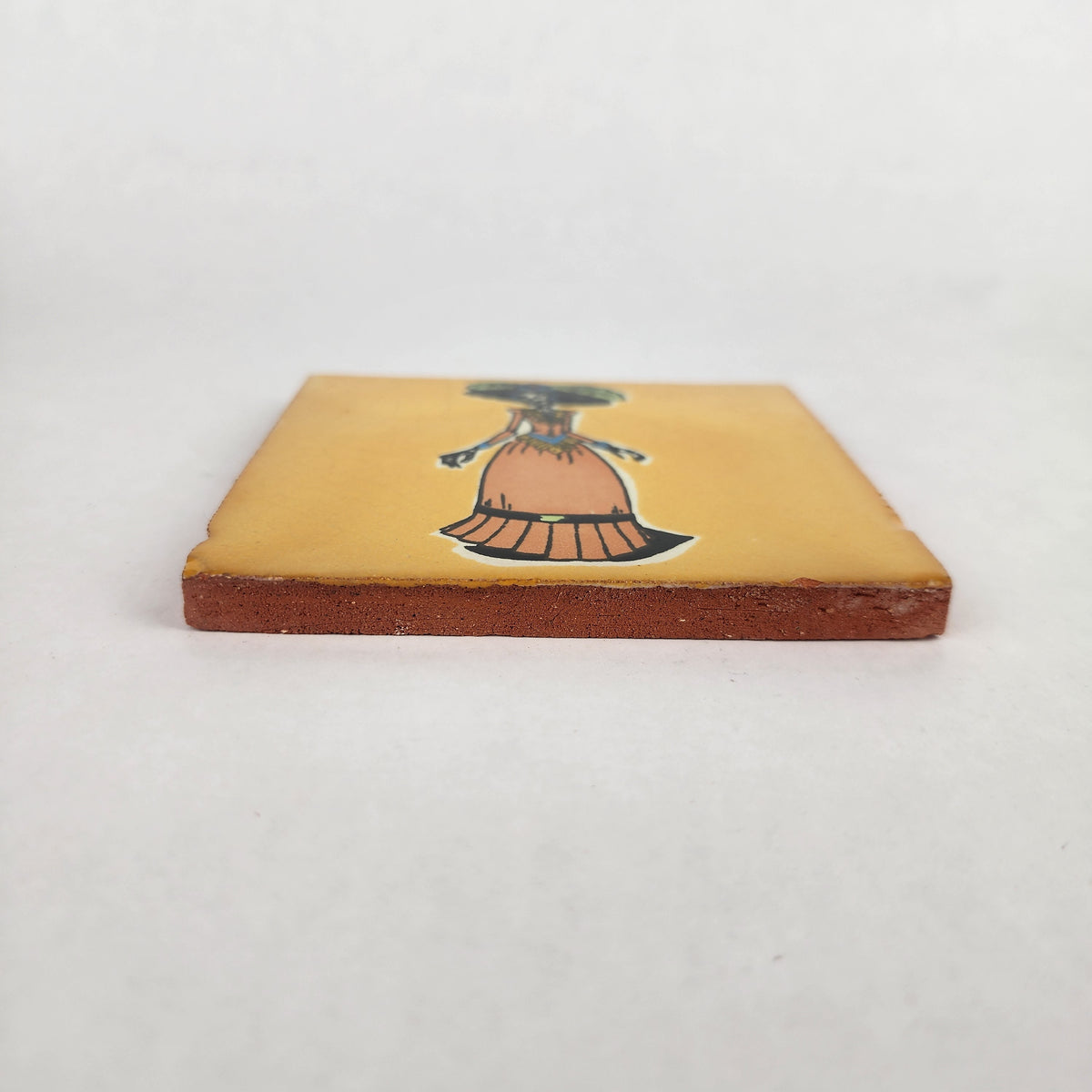 Side view of mustard yellow Catrina ceramic tile showing glazed surface and terracotta edge