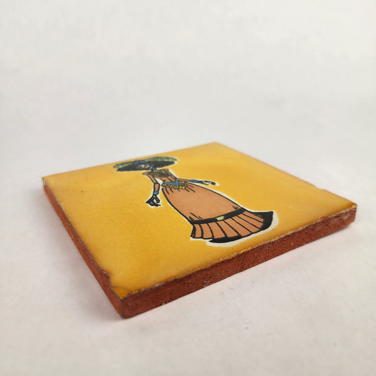 Angled view of mustard yellow Catrina ceramic tile showing glossy finish and terracotta edges