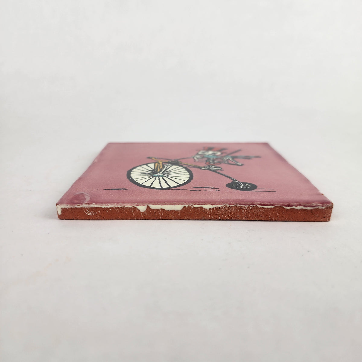 Side view of pink skeleton bicycle ceramic tile showing thickness and ceramic edge