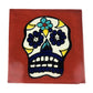 Floral sugar skull Mexican ceramic tile with red-brown background and blue flowers
