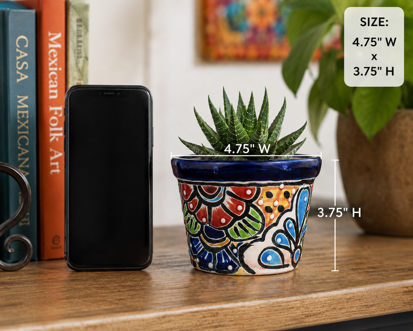 A small succulent in a hand-painted ceramic pot with a colorful Mexican-style pattern, shown on a wooden table next to a smartphone for scale, with size text overlay.